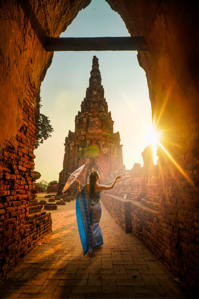 Mastering the First Impression: Your intriguing post title goes here A woman in traditional wear stands with an umbrella at a historic Ayutthaya temple during sunset.
